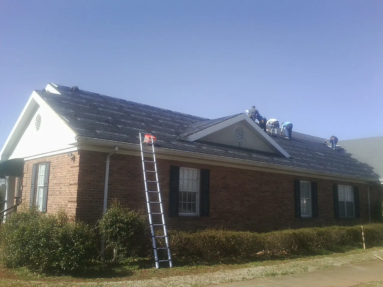 Crew tearing shingles off a brick ranch roof with a ladder set — Metal Roof Repair work by our crew in Tamassee