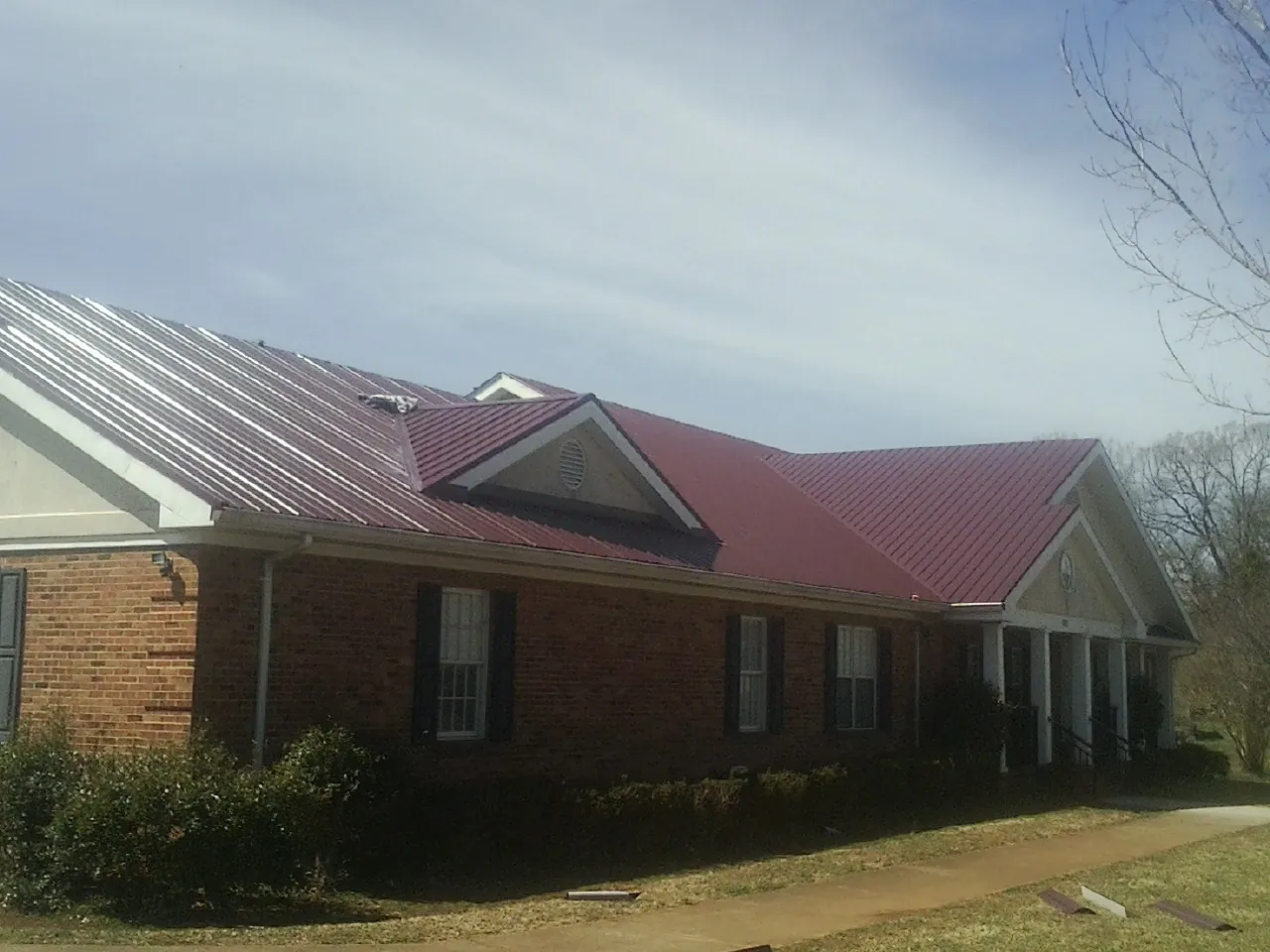 Red metal roof with gabled entries on a long brick building, from a Hail Damage Roof Repair job in Tamassee