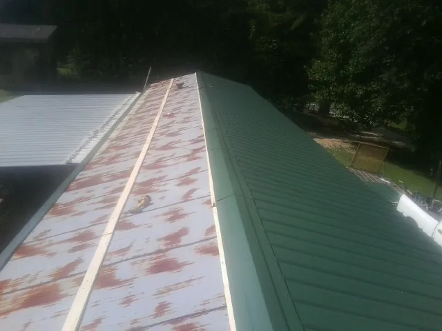 Old rusted panels beside newly installed green metal roofing — Wind Damage Roof Repair by Roofing Brothers in Tamassee