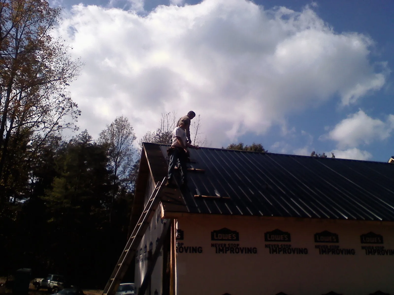 Roofer fastening dark metal panels high against a cloudy sky, from a Roof Inspection job in Tamassee