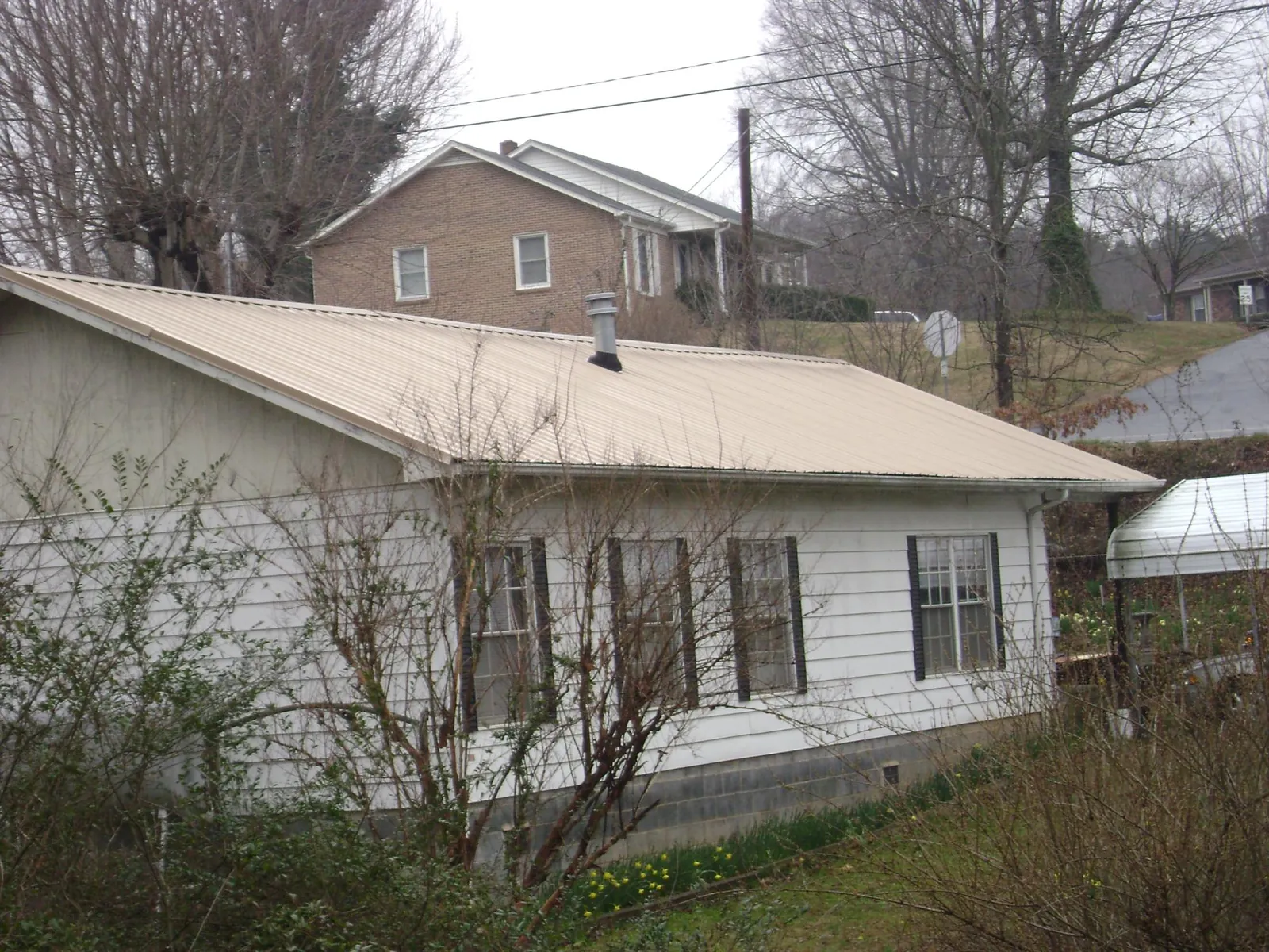 Tan metal roof on a white sided house set into a hillside — Commercial Roofing by Roofing Brothers in Tamassee