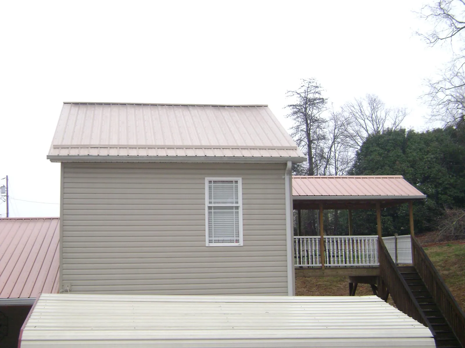 Tan metal roofs on a two story addition and attached porch, from a Roof Replacement job in Tamassee